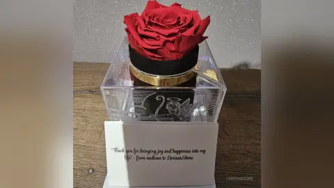 Elegant red rose in a clear luxury gift box with a gold rim and romantic thank you note on a wooden surface.