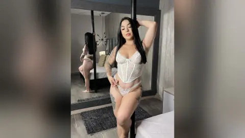 Young woman in white lace lingerie posing in a modern bedroom mirror reflection with a moody atmosphere.