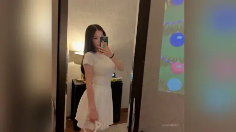 Young woman in a white summer dress taking a mirror selfie in a modern home setting.