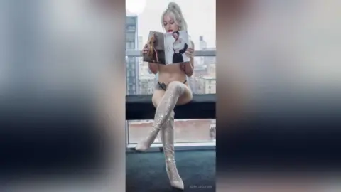 Blonde woman in sparkly silver thigh-high boots and lingerie sitting on a balcony overlooking a city skyline.