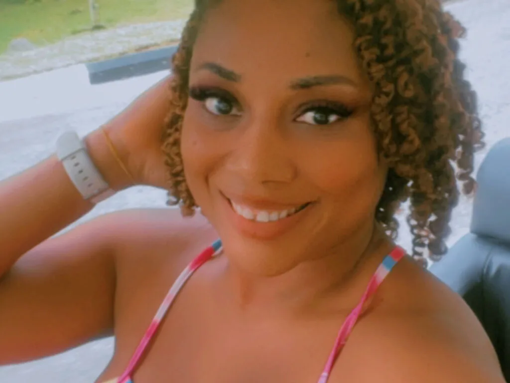 MandyJohn — MandyJohn smiles while wearing a pink patterned bikini top and posing outdoors.