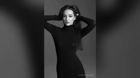 Elegant woman in a black ribbed turtleneck dress posing against a grey studio background in a moody portrait.
