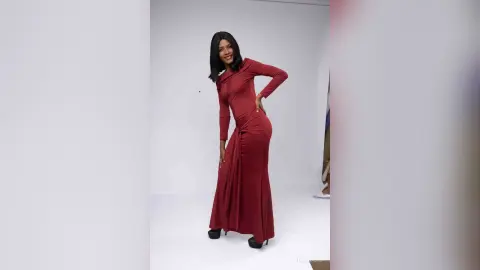 Smiling woman in a long-sleeved burgundy maxi dress posing in a bright studio setting.