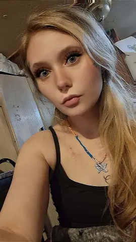 SummerBrookes poses close up, wearing a black tank top and a butterfly necklace, with her long blonde hair falling over her shoulder.