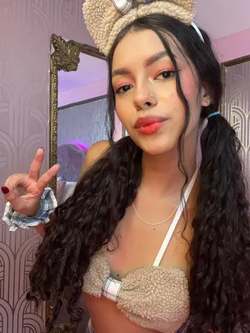 Young woman with long curly hair wearing a fuzzy teddy bear outfit and headband making a peace sign.