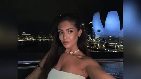 Young woman in a white strapless top enjoying a night out against a glowing city skyline background.