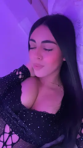 Young woman with long dark hair in a black sparkly cutout top posing under moody purple lighting.