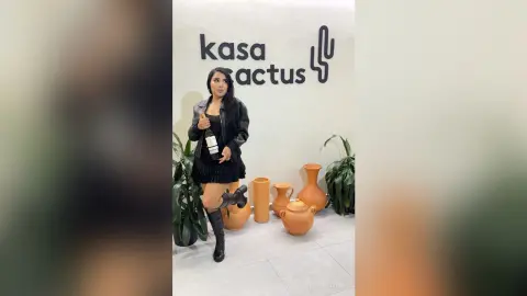 Stylish woman in a black dress and boots holding a wine bottle in a modern Kasa Cactus interior setting.