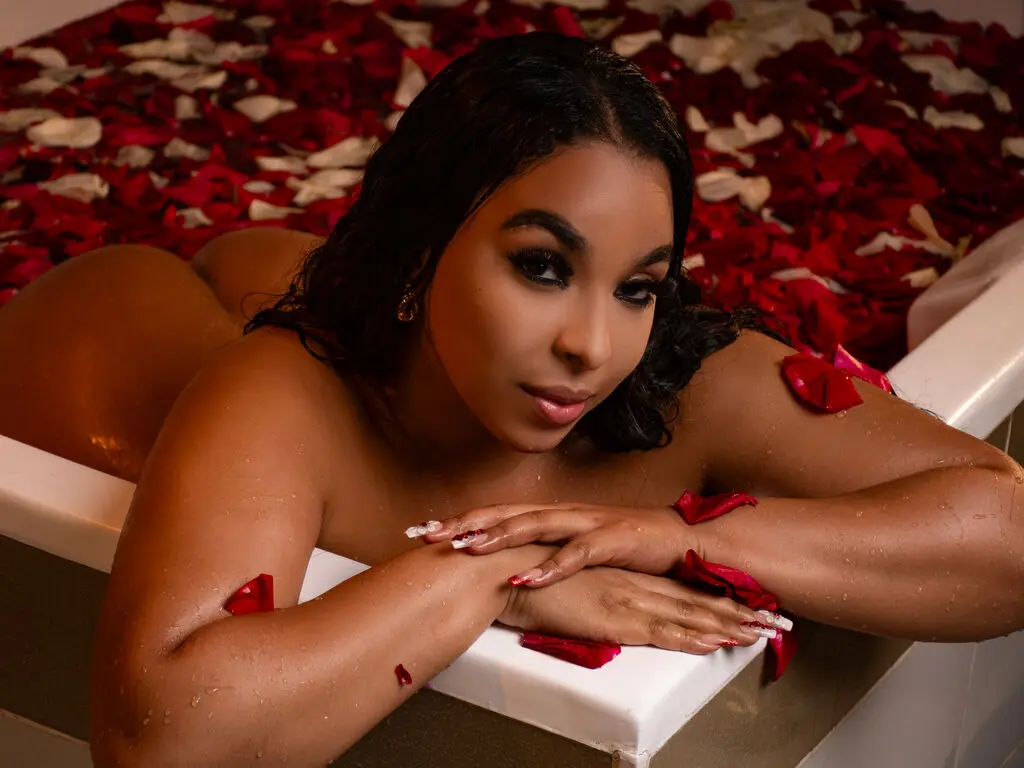 Glamorous woman with dark hair relaxing in a white bathtub filled with red rose petals for a romantic mood.
