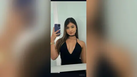 Young woman in a black V-neck dress taking a mirror selfie in a bright modern room.
