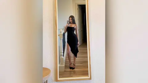 EvelynMills poses for a mirror selfie wearing a black spaghetti-strap dress with a high slit.