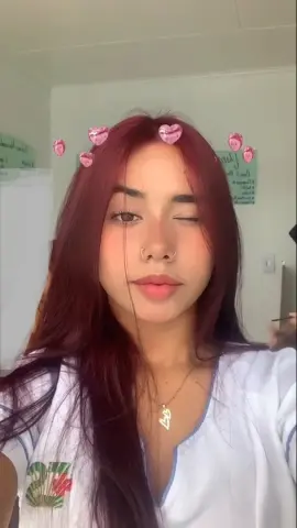 Young woman with reddish hair and nose ring wearing a white t-shirt in a bright indoor setting.