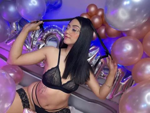 AnaWillsson poses in a black lace bra and matching garter, holding a black hair tie or strap behind her head amidst pink and silver balloons.