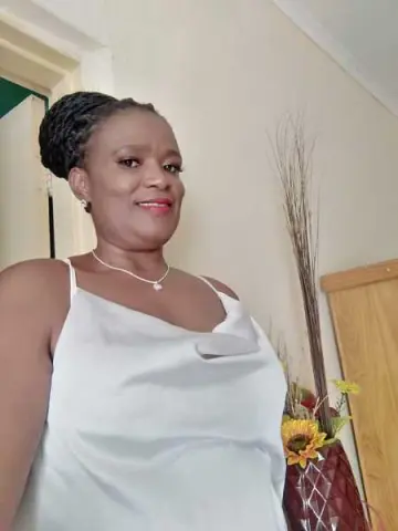 Smiling woman in a white satin camisole top posing indoors near a floral arrangement.