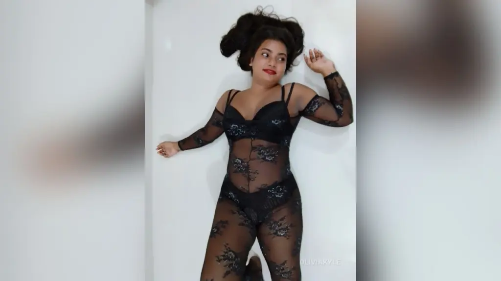 OliviaKyle — Woman in a black lace bodysuit posing against a white wall in a moody, elegant style.
