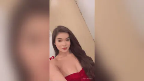 Smiling young woman in a red strapless top posing in a bright, minimalist indoor setting.
