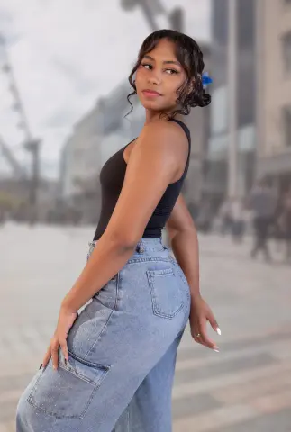 Young woman in a black tank top and light wash denim jeans posing in a city street setting.