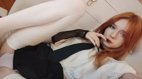 Redheaded woman in a white blouse and black skirt relaxing on a white sofa in a bright, cozy setting.