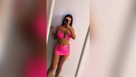 Young woman in a pink bikini set taking a mirror selfie in a bright room.