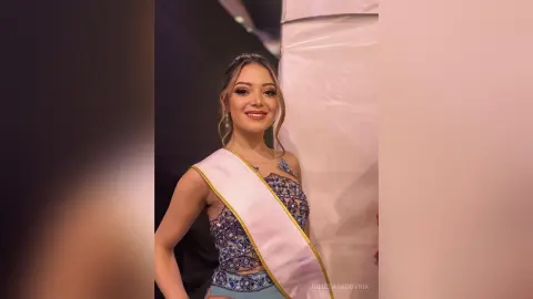 Smiling beauty queen in a sparkling blue pageant gown and white sash posing at a formal event.