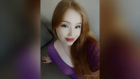 EpifaniaRalls poses with long red hair, wearing a purple low-cut top while looking at the camera.