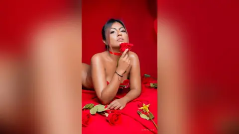 Glamorous woman in red setting lying on rose petals for a romantic and moody portrait.