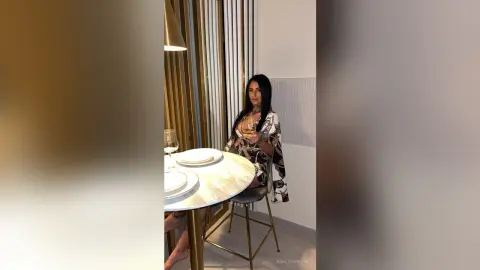 Elegant woman in a patterned black and white dress sipping wine at a marble table in a modern restaurant.