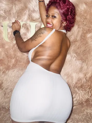 Smiling woman in a white backless dress relaxing on a soft pink faux fur background.