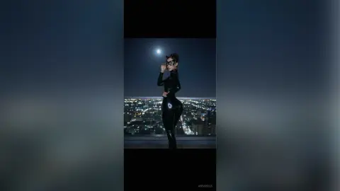 Woman in a sleek black bodysuit posing under the moon on a city rooftop at night.