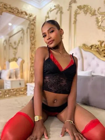 Glamorous woman in black lace lingerie and red stockings sitting on a bed in a luxury gold bedroom.