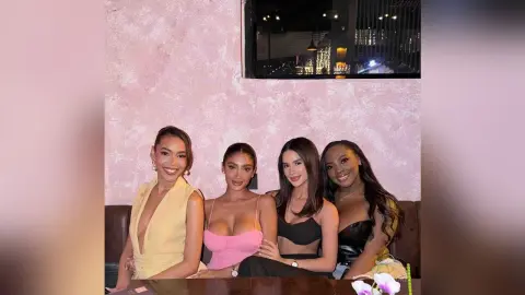 Four stylish women in elegant evening dresses smiling together at a chic lounge setting.