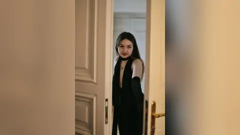 Elegant woman in a chic black outfit standing in a doorway with a sophisticated and moody atmosphere.