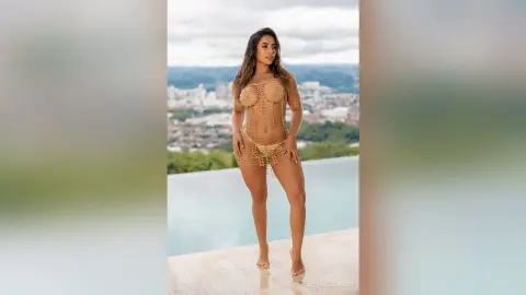 Glamorous woman in a gold crochet mini dress posing on a luxury rooftop pool terrace overlooking a city skyline.