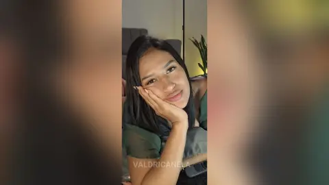 Smiling young woman in a dark green top posing for a cozy indoor selfie.