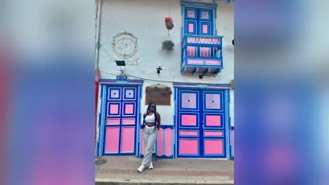 ValeryMei stands outside a blue and pink building wearing a white crop top and light grey pants.
