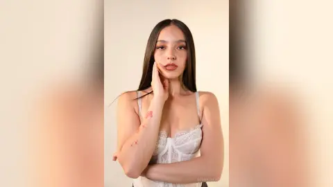 Young woman in a white lace corset top posing with a thoughtful expression against a neutral background.