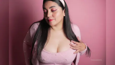 Young woman in a pink cardigan and headband posing against a soft pink background with a dreamy mood.