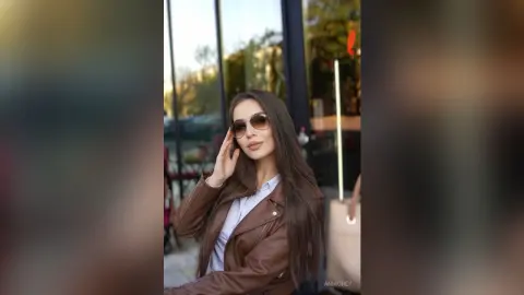 Stylish woman in a brown leather jacket and sunglasses posing outdoors in a chic urban setting.