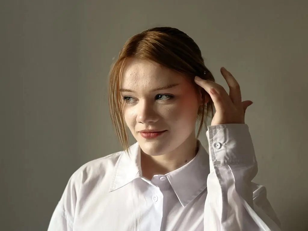 Young woman in a white button-down shirt looking thoughtful against a neutral gray background.