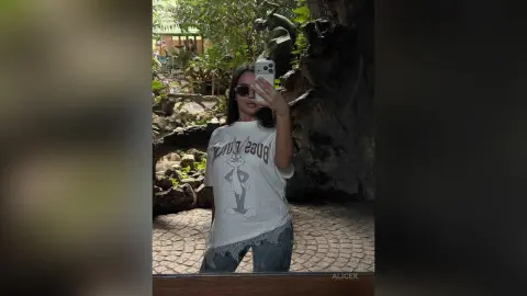 Young woman in a Bugs Bunny graphic t-shirt taking a casual selfie in a lush outdoor garden setting.