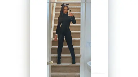 Stylish woman in an all-black outfit posing on a staircase in a modern home interior.