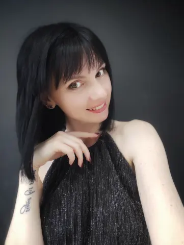 Smiling woman with black hair in a black halter top against a dark studio background.