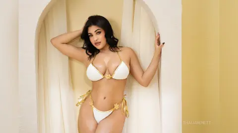 Beautiful woman in a white bikini posing in a bright, minimalist arched doorway setting.