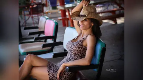 DrellaWolf — Stylish woman in a leopard print dress and straw cowboy hat relaxing in an outdoor patio setting.