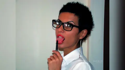 Stylish woman with short pixie hair and red lipstick wearing a white satin shirt in a bright indoor setting.