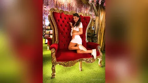 LauraRiveiro — LauraRiveiro sits on a large red velvet throne wearing a white crop top and white shorts.