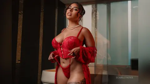 Glamorous woman in red lace lingerie and pearls posing in a modern bathroom setting with a confident mood.