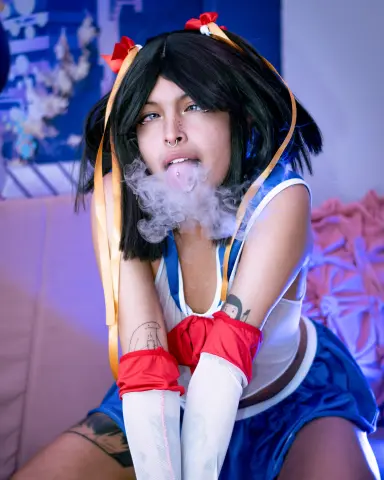 SakuraTao wears a blue and white sailor outfit with red gloves and a black bob wig while blowing smoke from her mouth.