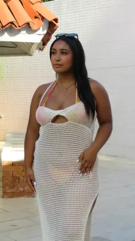 Young woman in a white crochet maxi dress standing outdoors in bright sunlight.