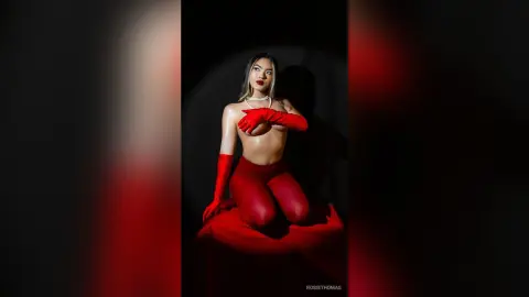 Glamorous woman in red gloves and matching outfit posing against a dark studio background with dramatic lighting.